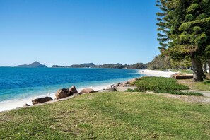 A coastal landscape with a clear blue sea, a sandy beach, and a grassy area with trees. - Miramar Coastal Escape (Corlette)