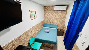 A compact room with a bed, a desk, a chair, a TV, an air conditioner, and a shower curtain. - Hostal San Andres Vive (San Andrés)