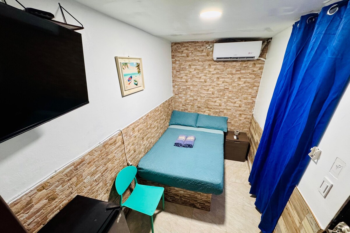 Habitació compacta amb llit, escriptori, cadira, televisió, aire condicionat i cortina de bany.
