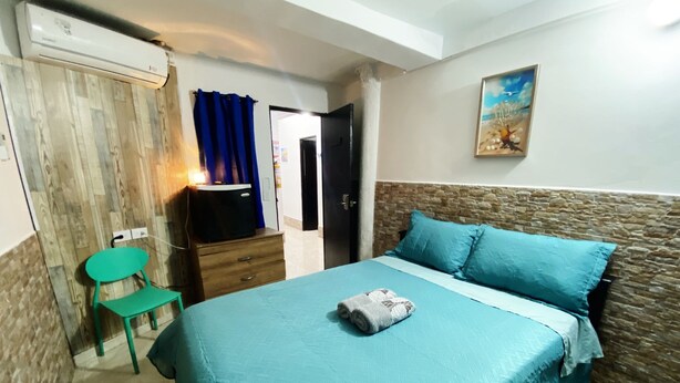 A bedroom with a bed, a chair, a dresser, and a painting on the wall. - Hostal San Andres Vive (San Andrés)