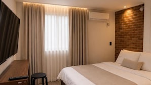 A hotel room with a bed, a desk, a chair, a TV, and an air conditioning unit. - Stay PAUSE (BUCHEON)