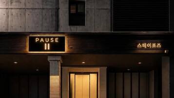 Eine Gebäudefassade mit einem 'PAUSE'-Schild, eine Betonkonstruktion und eine Tür.