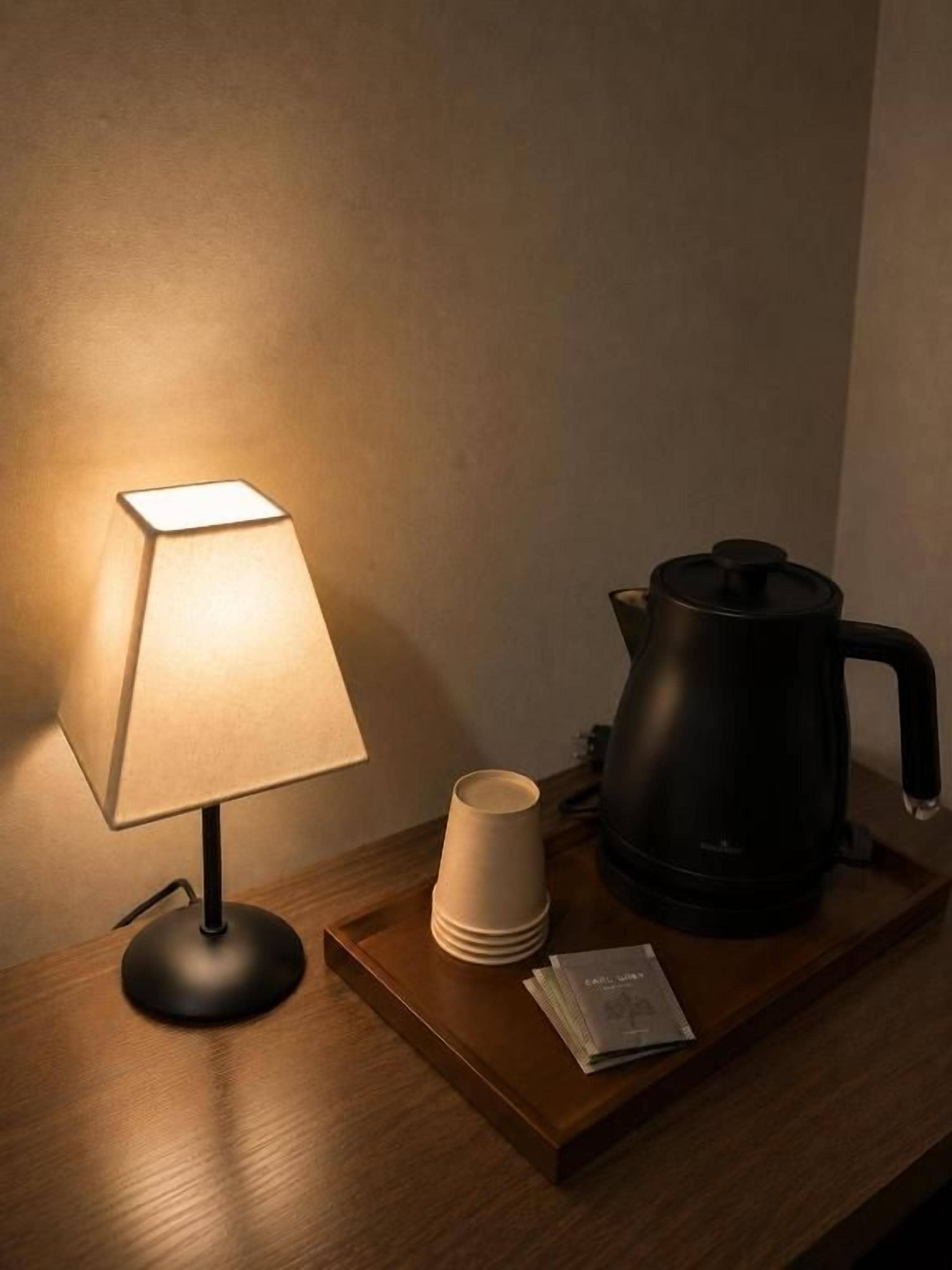 A bedside table with a lamp, a kettle, and some cups.
