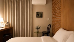 A hotel room with a bed, a desk with a lamp, a chair, a small table with a vase, and a picture on the wall. - Stay PAUSE (BUCHEON)