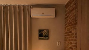 A hotel room with a bed, a chair, a table with a lamp, an air conditioning unit, and a brick wall. - Stay PAUSE (BUCHEON)