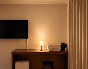 Camera d'albergo con TV a schermo piatto fissata al muro, una scrivania con lampada, una borsa e una macchina da caffè.