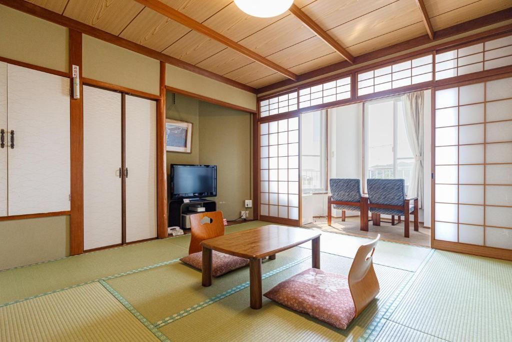 Une pièce de style japonais traditionnel, avec un sol recouvert de tatamis, une télévision, une table et des portes coulissantes.