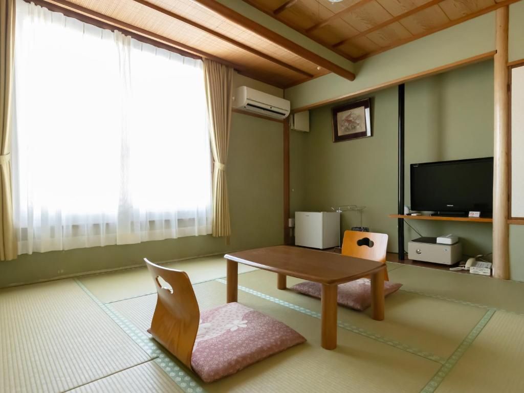 Une pièce de style japonais traditionnel, avec un sol recouvert de tatamis, une petite table basse, un téléviseur et un petit meuble.