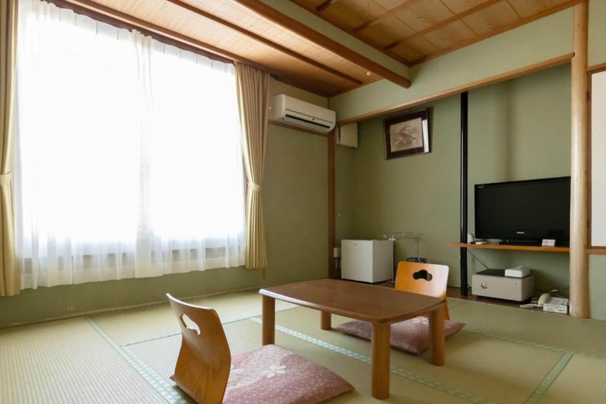 A traditional Japanese-style room with tatami flooring, a low table, a television, and a small cabinet.