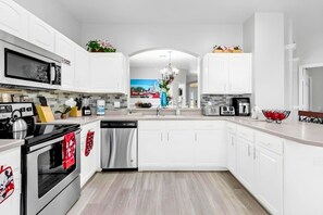A modern kitchen with white cabinetry, stainless steel appliances, and a view into the dining area. - 7BR Windsor Hills Heated Pool Game Room NearDisney (Kissimmee)