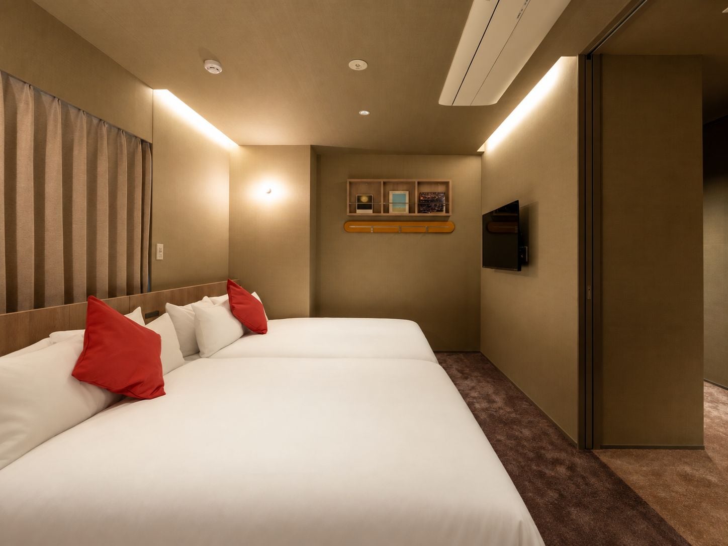 Habitación de hotel con una cama grande, un televisor de pantalla plana montado en la pared y un pequeño estante con objetos.