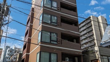 A multi-story building with a modern architectural design, featuring balconies on each floor and a visible entrance with a ramp.