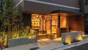 A modern hotel entrance with a glass facade, outdoor seating area, and a sign indicating 'Sumy Asakusa South'.