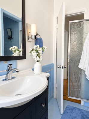 A bathroom with a white sink, a mirror, a vase with white flowers, a towel, and a shower area. - RETRO 2 BED 1.5 BATH - HISTORICAL HANCOCK PARK - NEAR WEHO (Los Angeles)