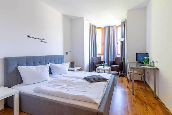 A hotel room with a bed, a desk, a chair, and a window with curtains. - Hotel Zum Dorfbrunnen (Schleusingen)