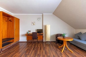 A room with a wooden wardrobe, a desk with a computer, a chair, a sofa, and a small table with a plant. - Hotel Zum Dorfbrunnen (Schleusingen)