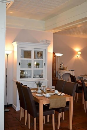 A dining area with a wooden table set for four, surrounded by chairs. A white cabinet with glass doors is visible in the background. - Hotel Zum Dorfbrunnen (Schleusingen)
