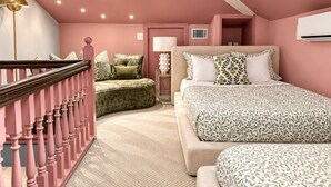 Une chambre avec un canapé incurvé, un lit avec une literie à motifs, une table de chevet avec une lampe et un escalier avec des balustrades roses.