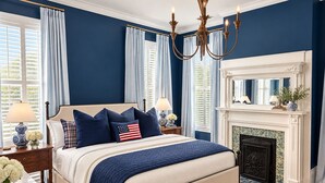 Une chambre à coucher avec un lit, des tables de chevet, un lustre, une cheminée et une vue sur l’extérieur.