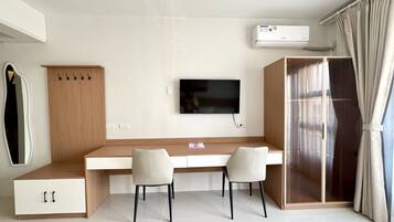 A modern bedroom with a bed, a desk, two chairs, a TV, and an air conditioning unit.