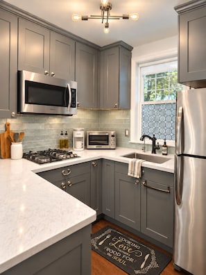 A modern kitchen with grey cabinets, stainless steel appliances, and a window with a blue-tiled backsplash.