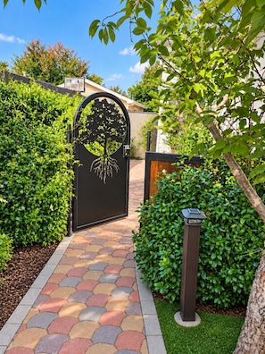 A gated entrance with a decorative tree design, a paved pathway, and well-maintained hedges.