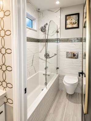 Un baño moderno con ducha envuelta en vidrio, inodoro blanco y pared de mármol.