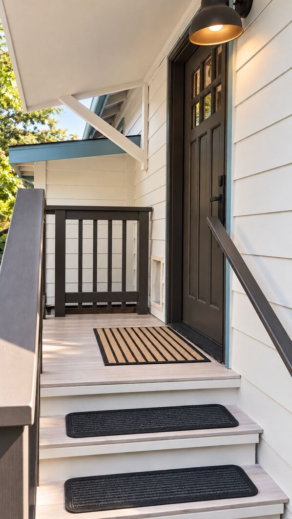 A house entrance with a dark front door, a light-colored porch, and a black metal railing.