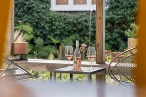 A table with two wine glasses and a bottle, set against a backdrop of greenery. - Desert Muse by Homello (Auckland)
