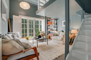 A spacious living room with a large window, a bookshelf, a sofa, and a staircase. - Desert Muse by Homello (Auckland)