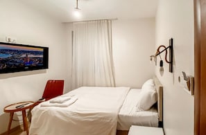 Hotellihuone, jossa on sänky, työpöytä, tuoli, seinälle asennettu televisio ja ikkuna, jossa on verhot.