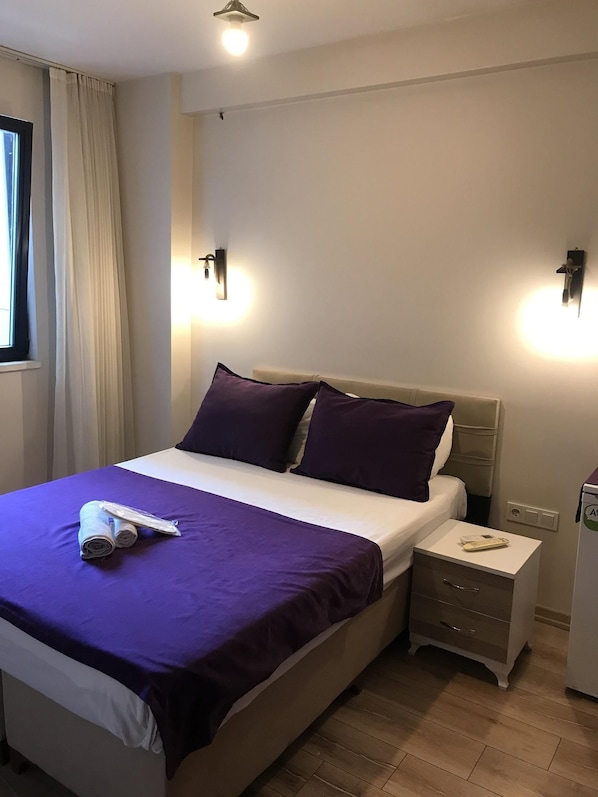Hotellihuone, jossa on sänky, yöpöytä, lamppu ja ikkuna, jossa on verhot.