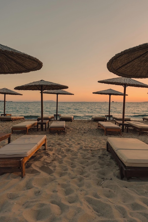 A beach with sun loungers and thatched umbrellas. - Nikos & Maria Studios (Naxos)