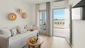 Een moderne woonkamer met een bank, een ronde houten tafel met fruit en een fles, en een balkon met uitzicht op zee.