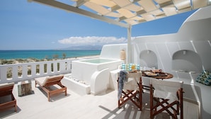 Een terras met uitzicht op zee, een jacuzzi en een eettafel met stoelen.
