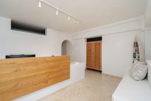 A reception area with a wooden reception desk, a white couch, and a bookshelf. - Nikos & Maria Studios (Naxos)