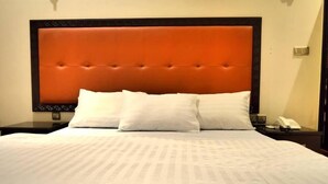 Una cama bien hecha con cabecera, dos almohadas y una mesita de noche con un teléfono.