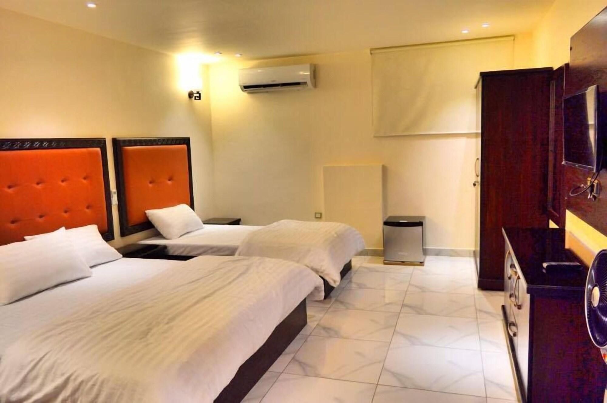 A hotel room with two beds, a wall-mounted air conditioner, a waste bin, and a television on a wooden cabinet.