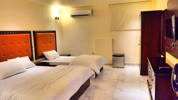 Habitación de hotel con dos camas, aire acondicionado de pared, un cesto de basura y un televisor sobre un mueble de madera.