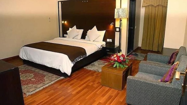 Ett hotellrum med en stor säng, ett nattduksbord, en soffa och ett litet bord med en vas med blommor.