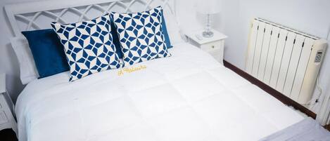 A bed with a white headboard, two pillows with a geometric pattern, and a bedside table with a lamp.
