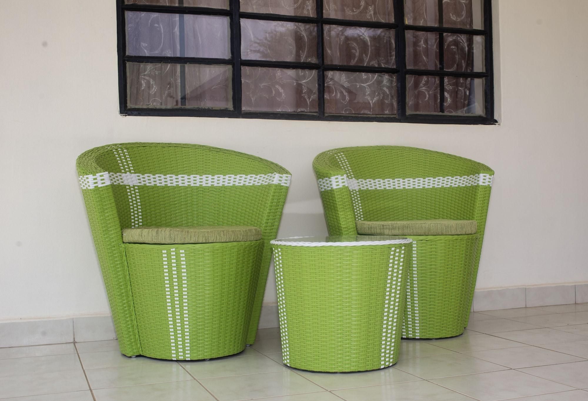 Three green wicker chairs with white decorative trim, positioned against a white wall with a window above.