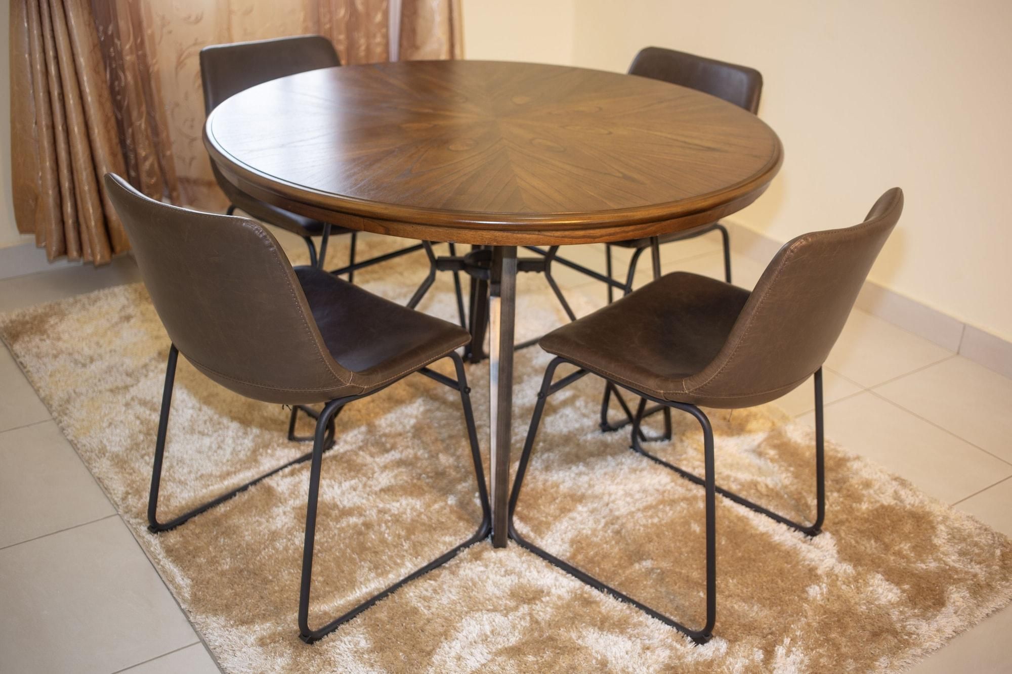 A round wooden table with four chairs, a brown shaggy rug, and a tiled floor.