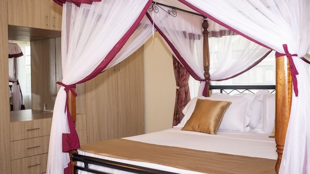 Ein Himmelbett mit Holzgestell, weißer Bettwäsche und einem goldenen Kopfkissen.