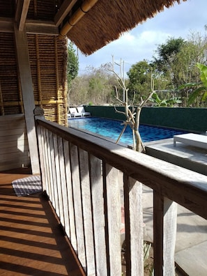 Um deck de madeira com piscina, um telhado de palha e vista para o verde ao redor.
