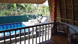 A pool area with a wooden deck, a chair, and a thatched roof structure. - Honeybee Huts (Lembongan Island)