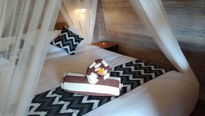 A bed with a patterned bedspread, a pillow, and a towel with a flower. - Honeybee Huts (Lembongan Island)