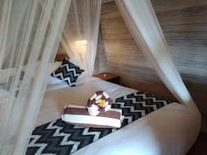 Uma cama com colcha estampada, um travesseiro e uma toalha com flor.