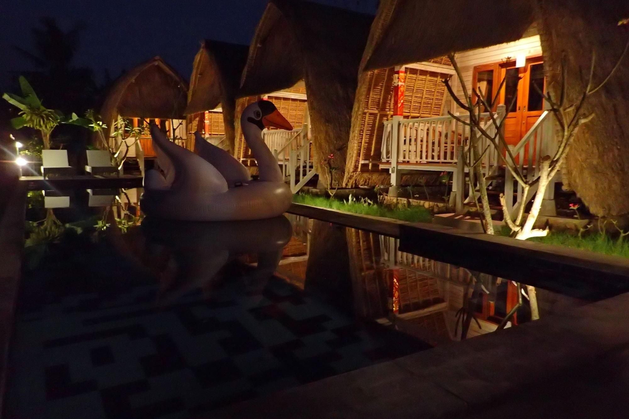 A nighttime view of a resort with overwater bungalows, a swimming pool, and a reflection of the bungalows in the water.
