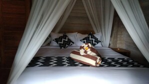A bed with a canopy, pillows, and a decorative item on the bed. - Honeybee Huts (Lembongan Island)